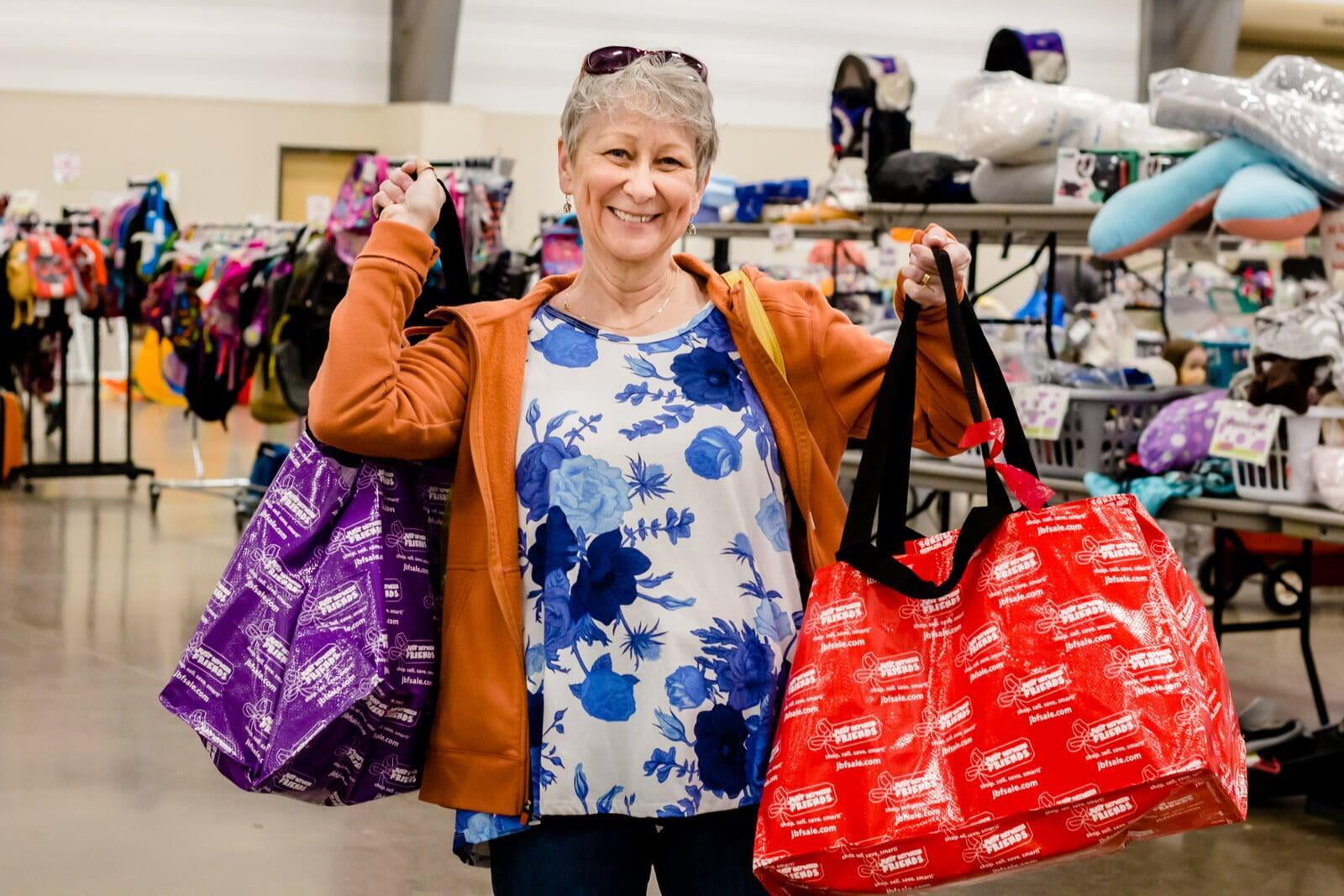 A proud grandma holds up 2 JBF shopping bags, one in each hand for each grandchild.